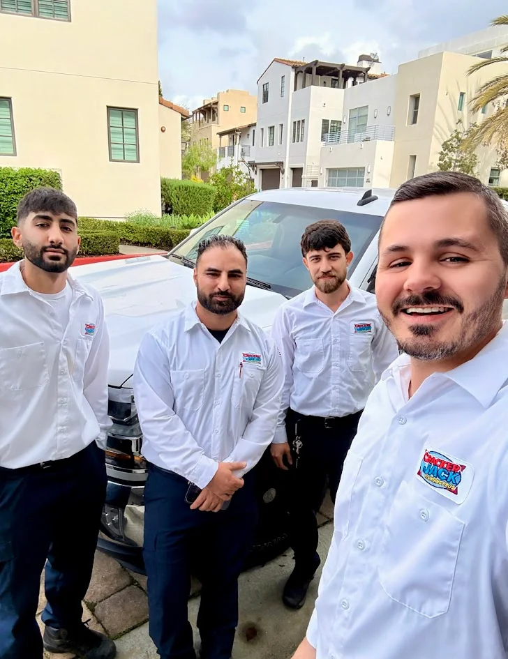 Four people wearing CrackerJack shirts beside a white vehicle outdoors.